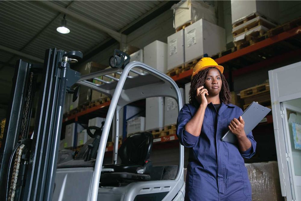 Logistics coordinator on the phone beside a forklift in a warehouse